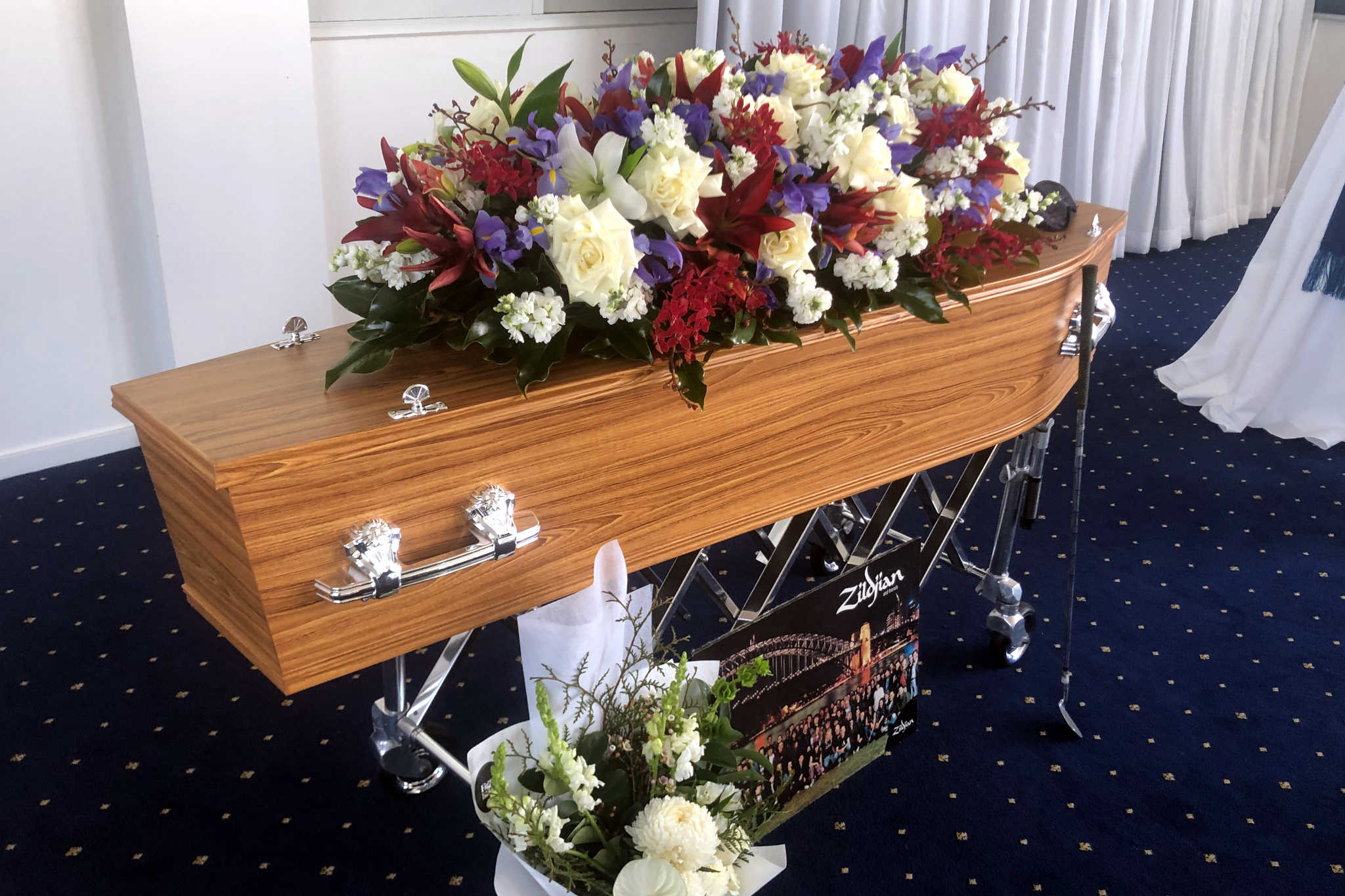 A wooden coffin with red, white and purple flowers on top